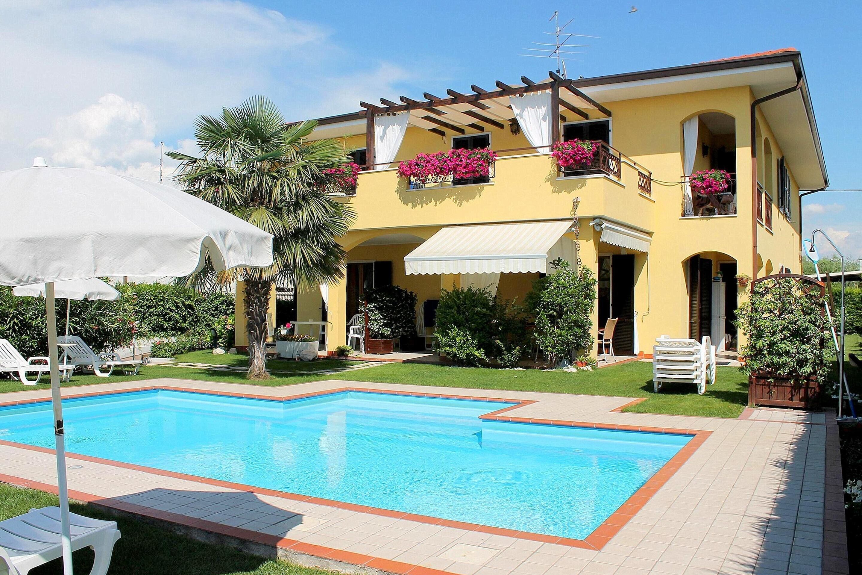 A yellow villa with a swimming pool, outdoor furniture, and a pergola with white curtains.
