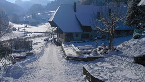 Un pueblo cubierto de nieve con un edificio destacado de techo pronunciado, rodeado de árboles cargados de nieve y un cielo despejado.