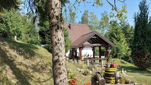 A rustic wooden structure with a sloped roof, surrounded by lush greenery and a clear sky.