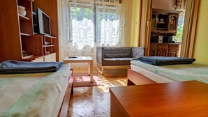 A room with two beds, a wooden table, a TV, and a small table with a remote control.