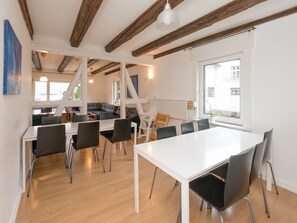 A modern interior with a white table and chairs, wooden beams, a large window, and a view of the outside. - Holiday Home in Dreislar Near the ski Area (Medebach)