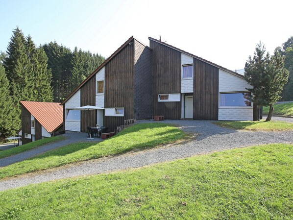 A modern two-story building with a sloped roof, a gravel driveway, and a small patio area with outdoor seating. - Splendid Holiday Home in Untervalme near Ski Area (Bestwig)