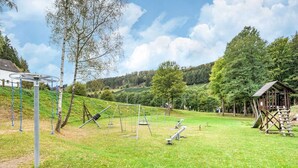 A playground with swings and a climbing structure, surrounded by trees and a grassy area. - Splendid Holiday Home in Untervalme near Ski Area (Bestwig)