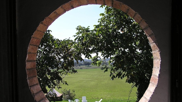 A view through a circular window of a swimming pool surrounded by a grassy lawn and trees. - Belvilla by OYO I Granai (Bagnoregio)