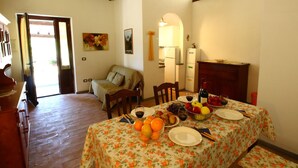 A dining area with a table set for two, featuring a floral tablecloth, plates, cutlery, and a bowl of fruit. - Belvilla by OYO I Granai (Bagnoregio)