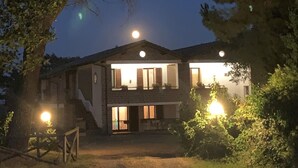 A two-story house with a visible staircase leading to the upper floor, surrounded by trees and a well-lit front yard. - Belvilla by OYO I Granai (Bagnoregio)