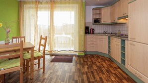 A kitchen with wooden cabinets, a dining table with chairs, and a window with curtains. - Gemutliches Ferienhaus in Sebnitz (Sebnitz)
