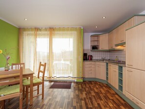 A kitchen with wooden cabinets, a dining table with chairs, and a window with curtains. - Gemutliches Ferienhaus in Sebnitz (Sebnitz)