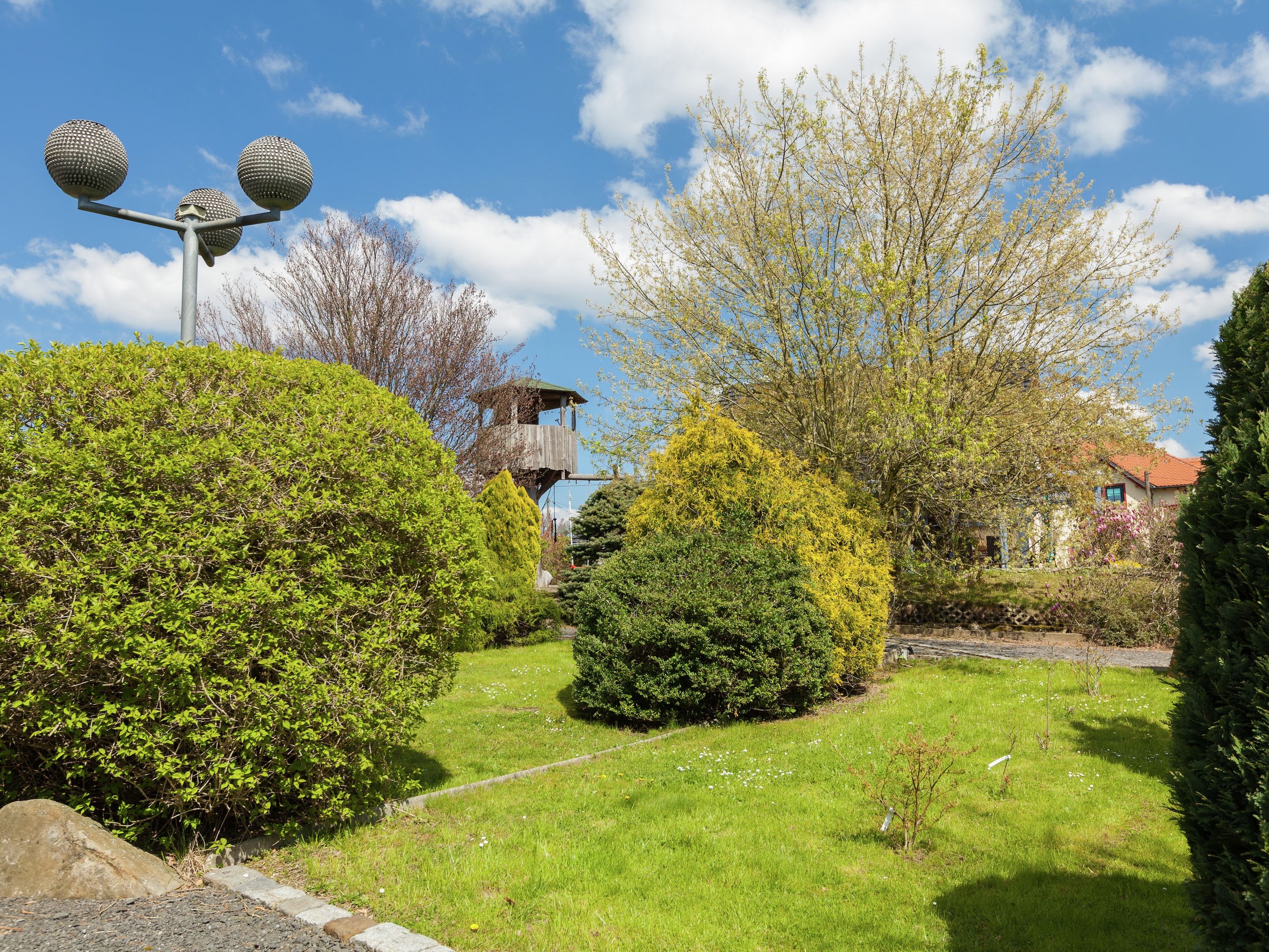 A well-maintained garden with neatly trimmed hedges, a clear pathway, and a traditional building with a red roof.
