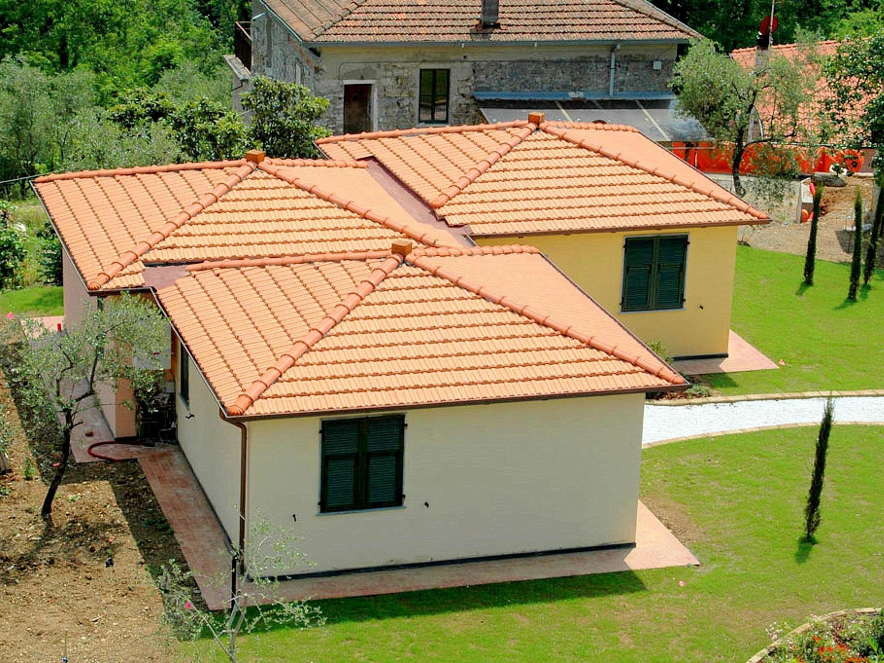 Deux maisons de plain-pied aux toits recouverts de tuiles orange, entourées de verdure et baignées par un ciel dégagé.