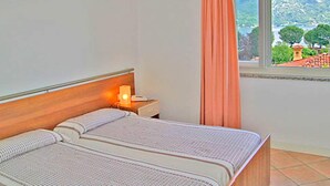 A bedroom with a bed, a nightstand, and a window with curtains. - Belvilla by OYO Bilo Garden Due Bis (Cannobio)