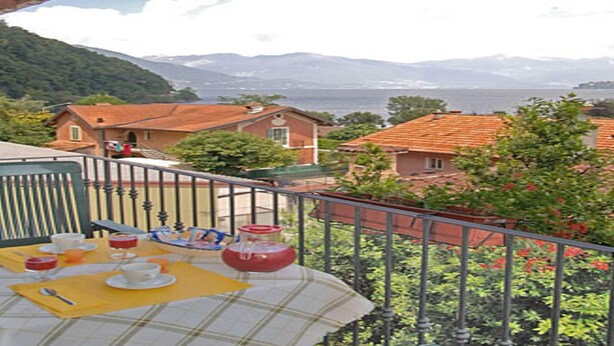 A balcony with a table set for breakfast, overlooking a coastal village with houses and mountains in the background. - Belvilla by OYO Bilo Garden Due Bis (Cannobio)