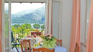 A balcony with a table and chairs, a view of a mountainous landscape, and a table with a vase of flowers. - Belvilla by OYO Bilo Garden Due Bis (Cannobio)