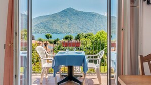 A balcony with a table and chairs, overlooking a lake and mountains. - Belvilla by OYO Studio Garden Uno Bis (Cannobio)