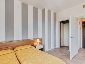 Ein Hotelzimmer mit Bett, Nachttisch, Lampe und einer Tür zu einem weiteren Raum.