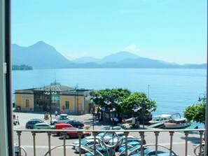 Vista de un lago con montañas al fondo, un estacionamiento con coches y un edificio de fachada amarilla.