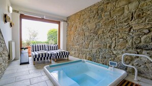 A stone-walled room with a pool, two striped sofas, and a bench.