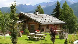 A log cabin with a sloped roof, surrounded by a well-maintained lawn and a wooden fence. - Dreamy Cottage in Bellamonte Italy with Hot Tub (Predazzo)