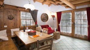 A wooden dining table with chairs, a basket of fruit, a bottle of wine, and a candle on a lace tablecloth. - Dreamy Cottage in Bellamonte Italy with Hot Tub (Predazzo)