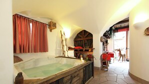 A rustic bathroom with a wooden bathtub, a red curtain, and a wooden bench. - Dreamy Cottage in Bellamonte Italy with Hot Tub (Predazzo)