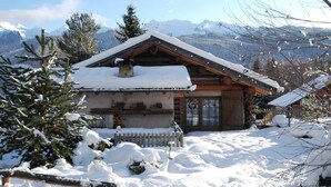 A wooden chalet with a snow-covered roof, surrounded by snow-covered trees and mountains in the background. - Dreamy Cottage in Bellamonte Italy with Hot Tub (Predazzo)