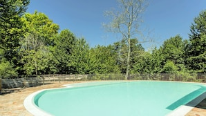 Une piscine rectangulaire, bordée d’un revêtement de sol en pierres, et entourée d’une clôture en métal et d’arbres.