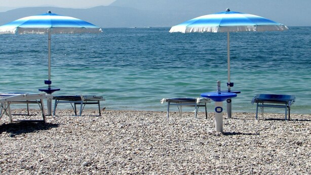 Une plage de galets avec deux parasols bleus et des chaises longues donnant sur la mer.