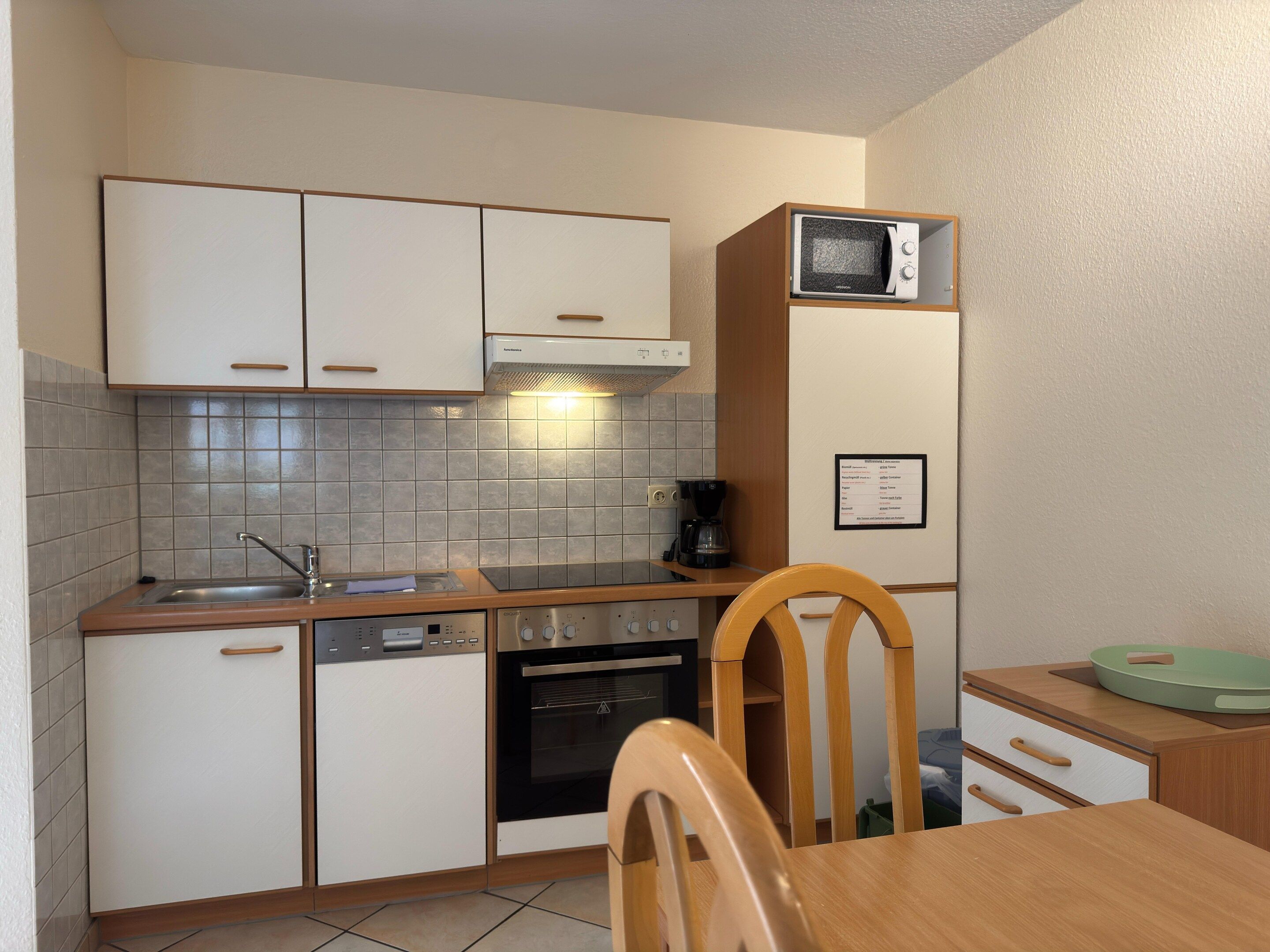 A compact kitchen with white cabinets, a microwave, a coffee maker, and a wooden dining table.