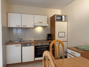 A compact kitchen with white cabinets, a microwave, a coffee maker, and a wooden dining table.