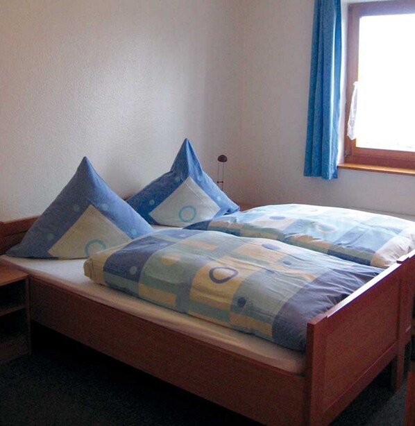 A bed with blue and white bedding, a wooden headboard, and a window with blue curtains.