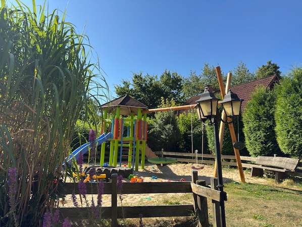 A playground with a slide and climbing structures, surrounded by trees and a wooden fence. - Holiday Home in the Teutoburg Forest (Brakel)