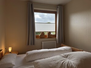 Una habitación de hotel con dos camas, una ventana con cortinas, una lámpara de noche y un radiador.