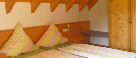 A bedroom with a wooden ceiling, a bed with striped bedding, and a wooden wardrobe.