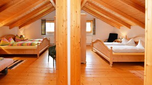 Ein Spiegelbild zeigt ein Schlafzimmer im Dachgeschoss mit Holzboden, zwei Betten, einer Heizung und einem Fenster mit Vorhängen.