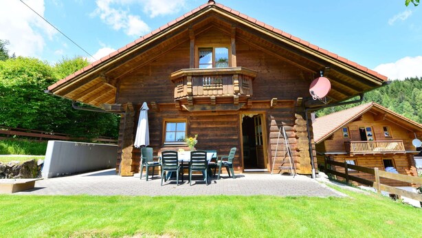 Eine Holzhütte mit Balkon, Sitzgelegenheit im Freien und Blick auf die Berge.