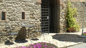 A stone building with a large arched doorway, outdoor seating with metal tables and chairs, and a potted plant near the entrance. - Holiday Home in Cortona (Cortona)