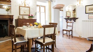 A dining area with a wooden table set for four, surrounded by chairs. There is a fireplace on the left, a wall-mounted telephone, and a mirror above the table. - Holiday Home in Cortona (Cortona)