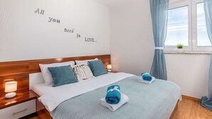Un dormitorio ordenado con una cama, almohadas, una mesita de noche con una lámpara y una ventana con cortinas.