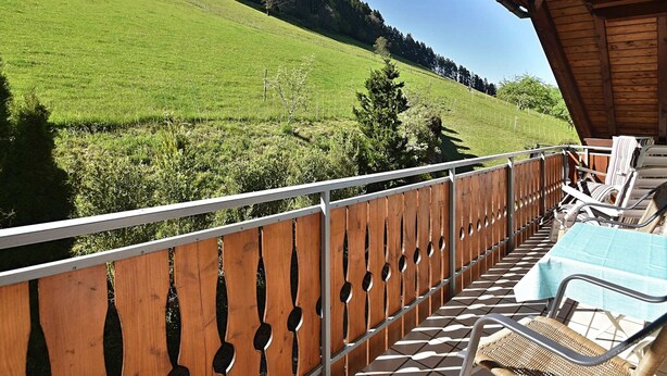 Un balcón de madera con vistas a una ladera verde y árboles.