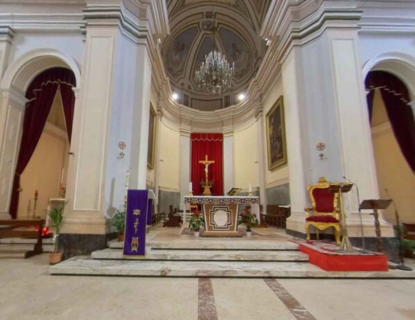A church interior with a central altar, pews, and a chandelier.