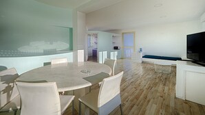 A modern living room with a round dining table, white sofas, and a flat-screen TV. - Belvilla by OYO Casa Zefiro (Santa Croce Camerina)