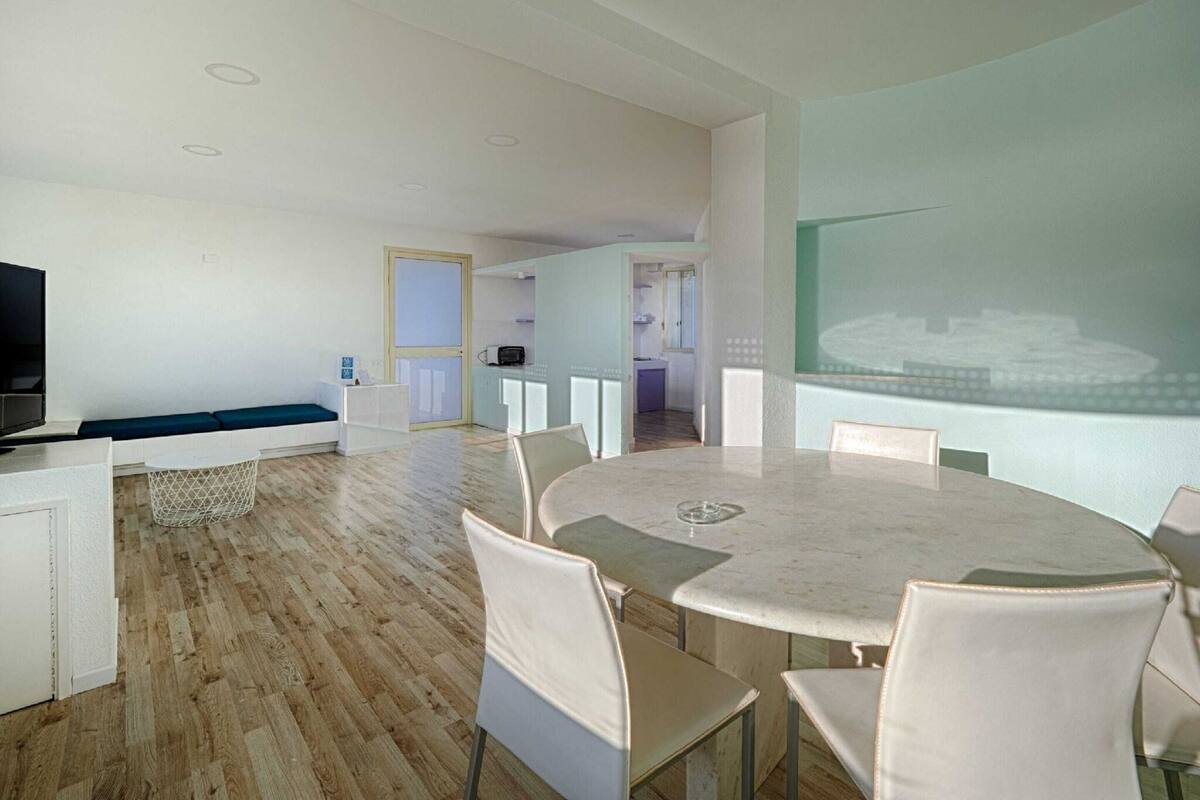 A modern living room with a round dining table, white chairs, a sofa, and a television.