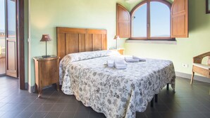 Un dormitorio con cama de madera, una mesita de noche, una lámpara y una ventana con contraventanas de madera.
