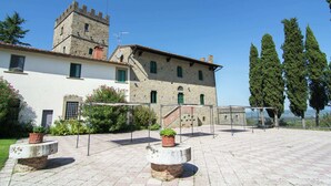 Un patio con un edificio de piedra que presenta una torre, plantas en macetas y un sendero pavimentado.