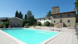 Una piscina con sillas de descanso, un edificio de piedra con una torre y un cielo azul despejado.