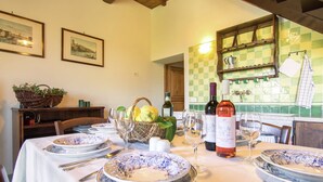 Una mesa de comedor dispuesta con platos, vasos y cubiertos, con una cesta de limones y una botella de vino sobre la mesa.