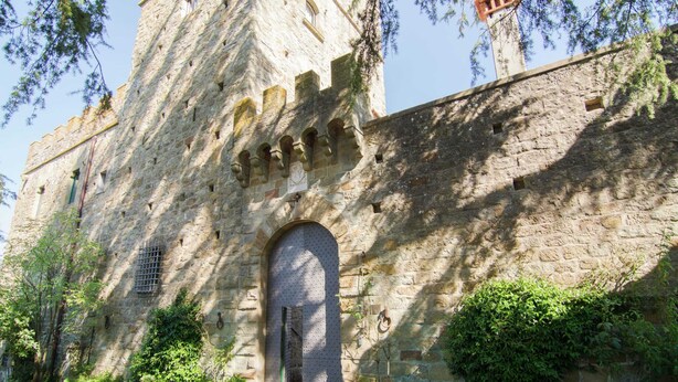 Un edificio histórico de piedra con un gran arco de entrada, una torre con almenas y un cartel sobre la entrada.