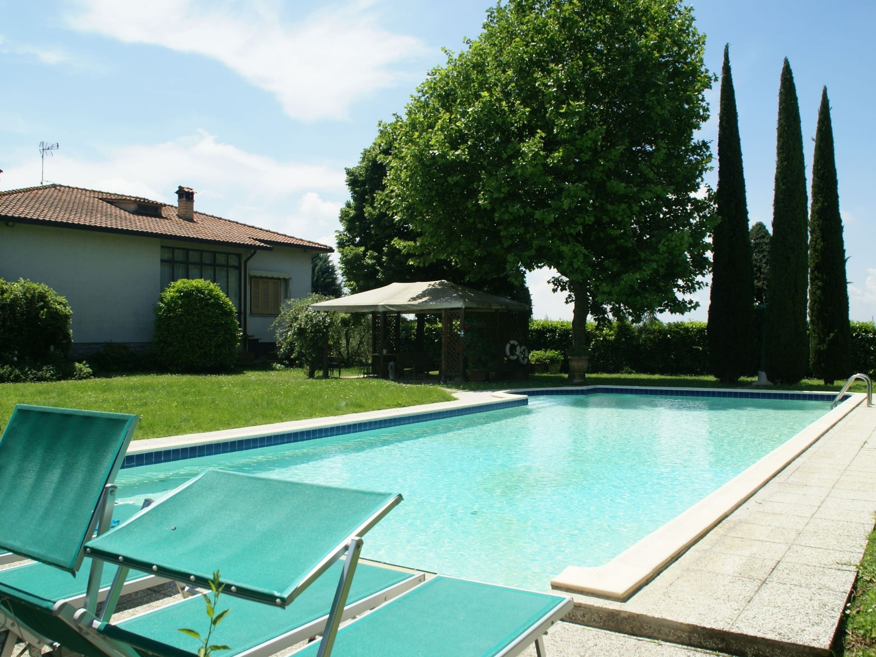 A swimming pool with lounge chairs, a gazebo, and a house in the background.