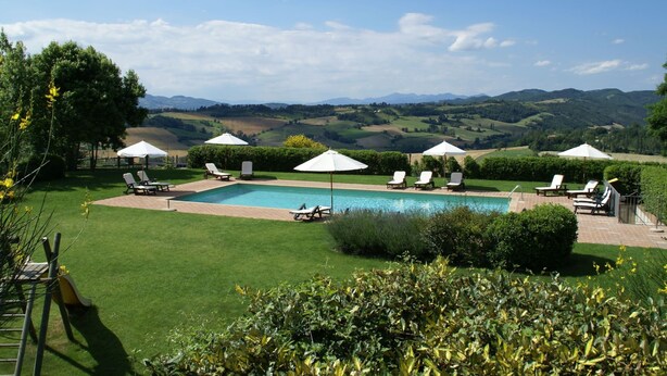 A pool area with lounge chairs and umbrellas, surrounded by well-maintained lawns and a scenic view of rolling hills.