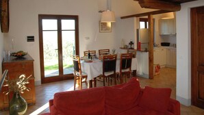 Een eethoek met een tafel voor vier personen, houten stoelen, een rode bank en een keuken op de achtergrond.